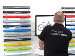 Mann mit dem Rücken, der an einem Computer ein Fahrraddesign bearbeitet. Farbige Folien im Hintergrund.