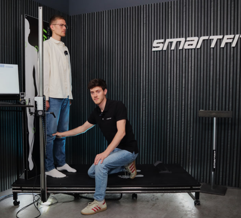 Person steht auf einer Plattform, während ein anderer seine Körpermaße nimmt.