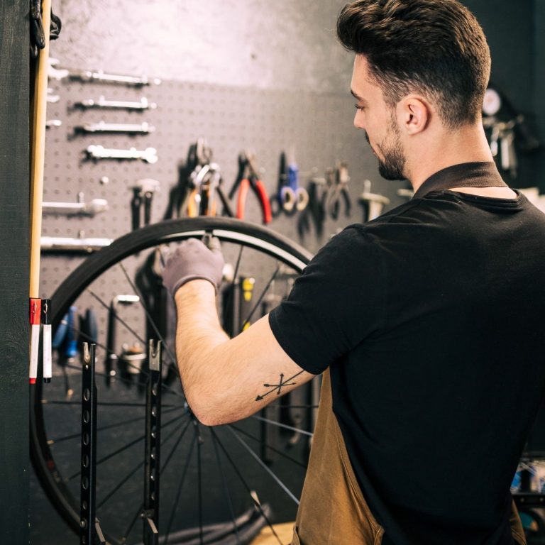 Ein Mechaniker arbeitet an einem Fahrradreifen in einer Werkstatt mit Werkzeugen im Hintergrund.